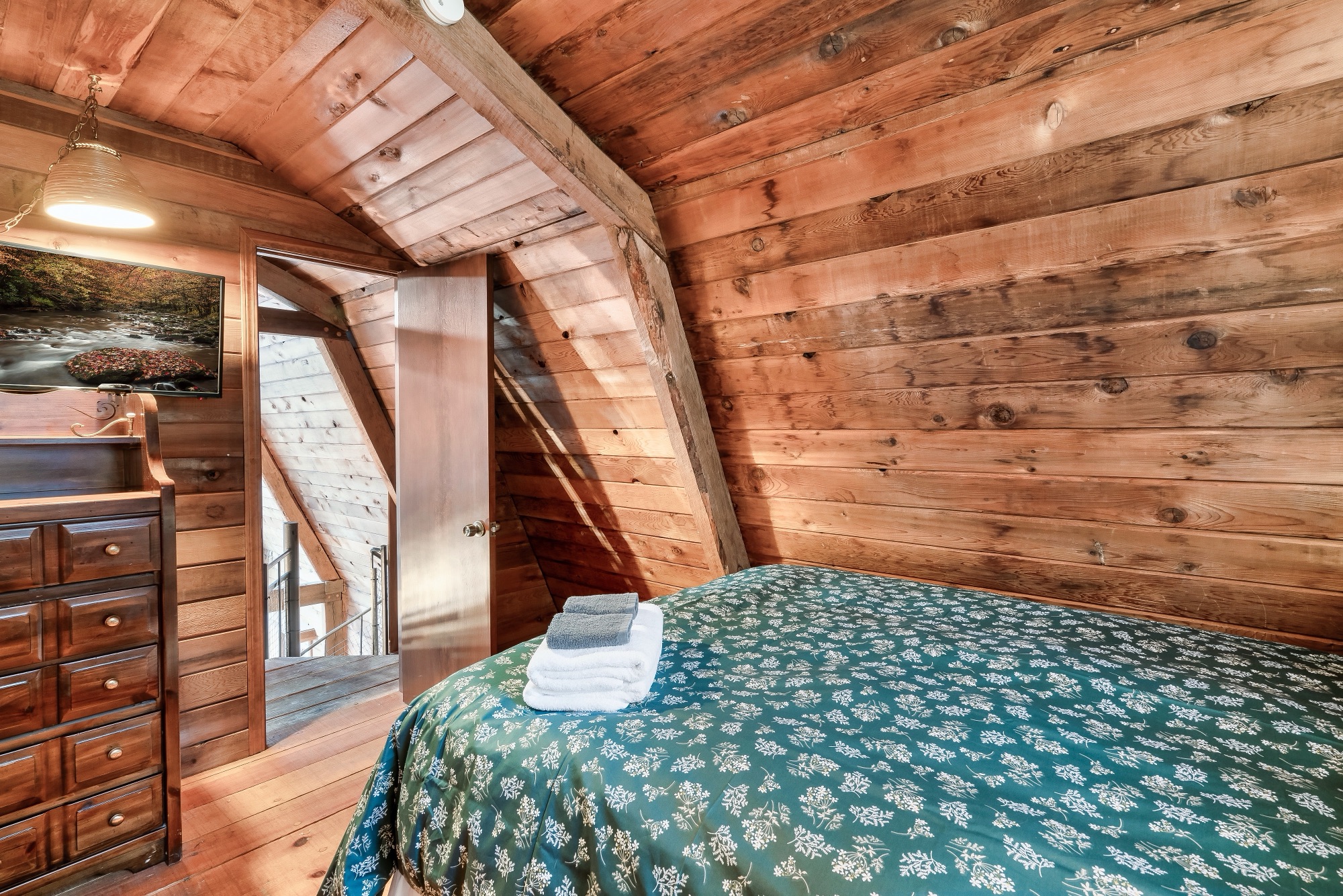 Rustic Retreat loft bedroom with a dresser, mounted TV, and a doorway opening to the loft landing